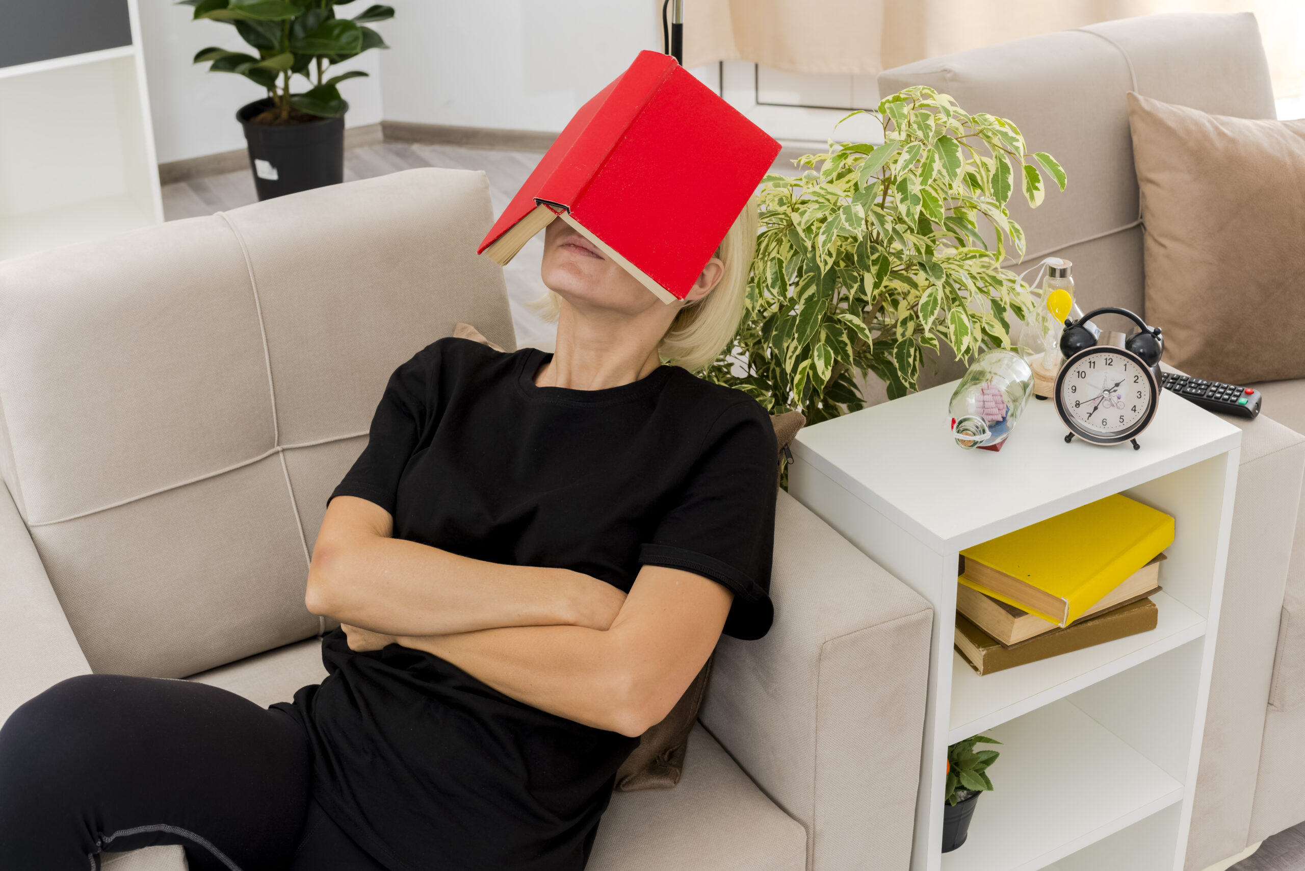 pleased beautiful blonde russian woman lying on armchair holding book on face and crossing arms inside design living room