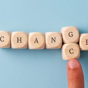 Word Change spelled on wooden dices with male finger replacing the letter G wit letter C to spell the word Chance. Over blue background.