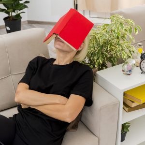 pleased beautiful blonde russian woman lying on armchair holding book on face and crossing arms inside design living room